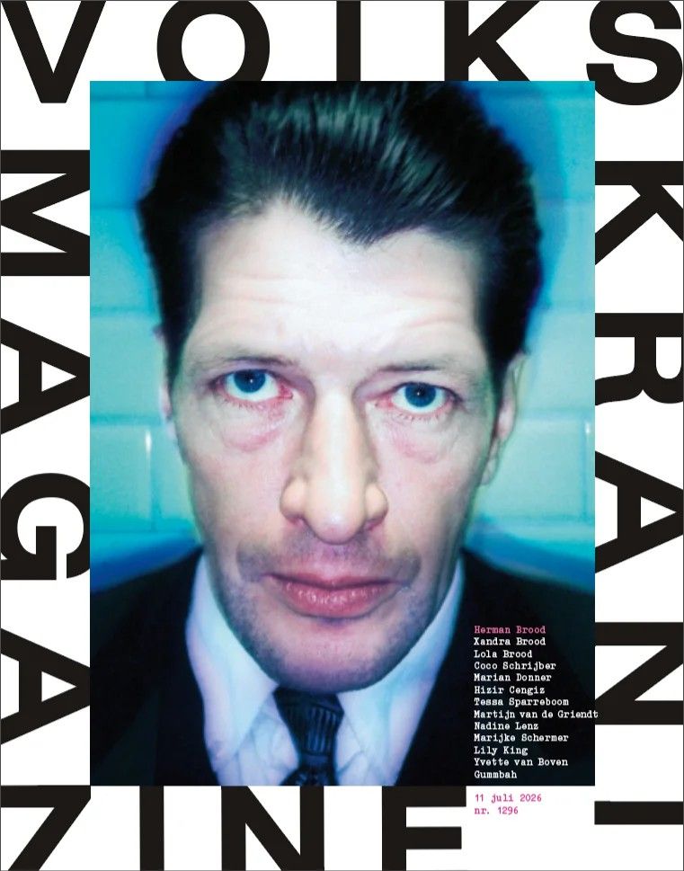 Magazine cover featuring a tightly cropped portrait photograph of a man with dark slicked-back hair and pale blue eyes, wearing a dark suit and striped tie, shot against a pale blue-teal tiled wall with flash lighting and a cool, bleached color cast.