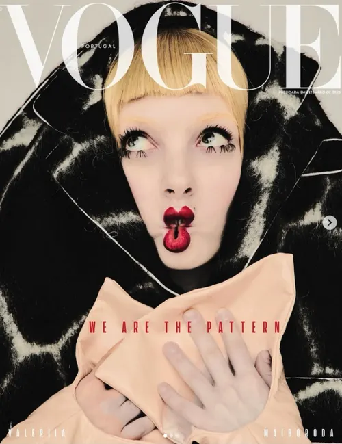 A Vogue Portugal magazine cover featuring a close-up portrait of a woman with blonde bangs and bold red lips against a black and white geometric patterned garment.